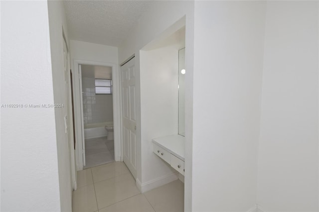 hallway with a textured ceiling and light tile patterned floors