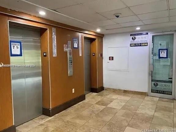 corridor with elevator and a paneled ceiling