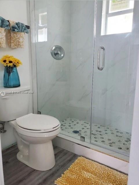 bathroom featuring hardwood / wood-style flooring, a shower with shower door, and toilet