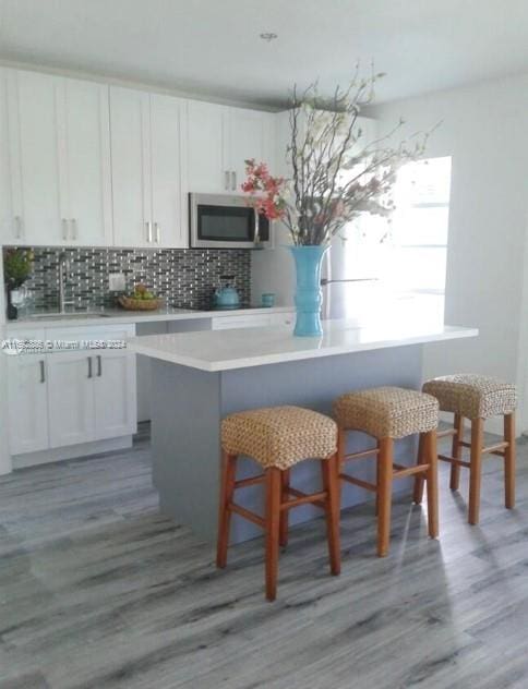 kitchen with white cabinetry, backsplash, sink, hardwood / wood-style floors, and a breakfast bar area