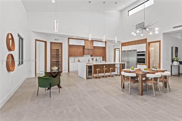 dining room featuring a high ceiling, wine cooler, an inviting chandelier, and sink