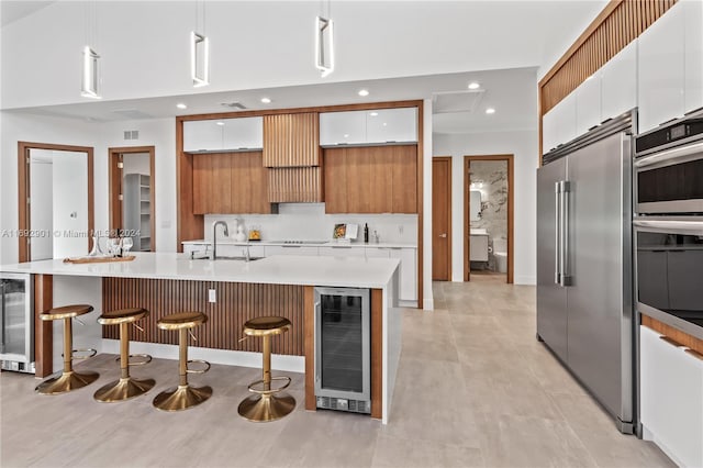 kitchen with a center island with sink, built in refrigerator, white cabinetry, a breakfast bar, and beverage cooler