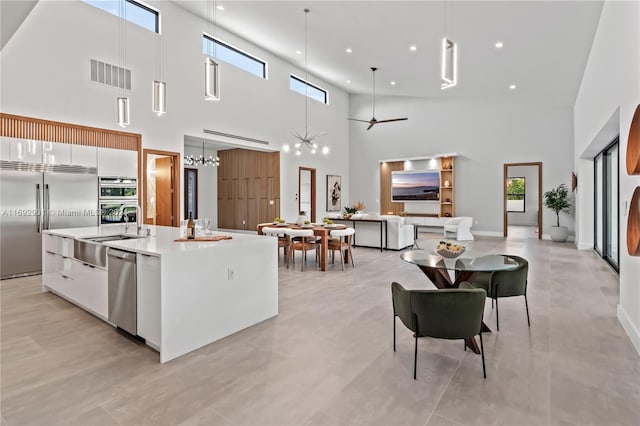 kitchen with stainless steel appliances, a high ceiling, white cabinetry, an island with sink, and pendant lighting