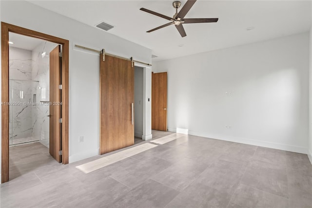 unfurnished bedroom with ensuite bathroom, a barn door, and ceiling fan