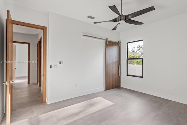 unfurnished bedroom with a barn door and ceiling fan