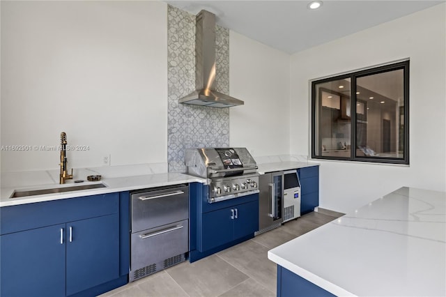 kitchen with light tile patterned flooring, light stone countertops, sink, blue cabinets, and wall chimney exhaust hood