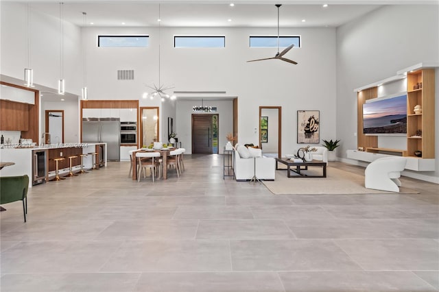 living room with wine cooler, light tile patterned floors, ceiling fan, and a towering ceiling