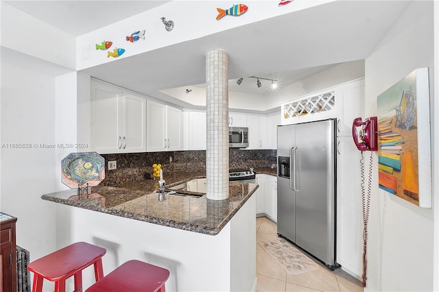 kitchen featuring kitchen peninsula, appliances with stainless steel finishes, decorative columns, white cabinets, and decorative backsplash