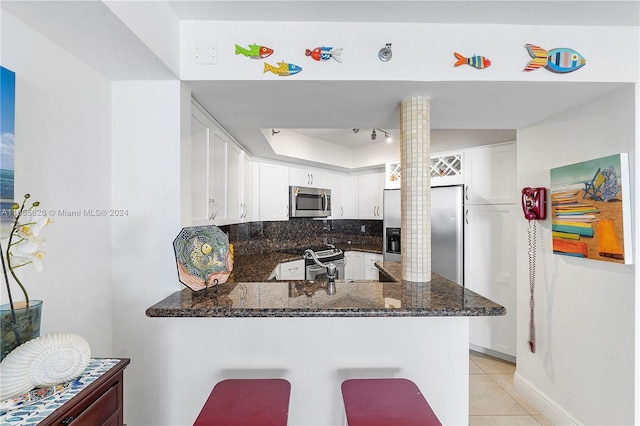 kitchen featuring dark stone countertops, white cabinetry, kitchen peninsula, and appliances with stainless steel finishes