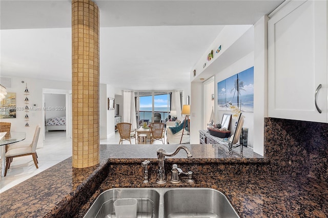 kitchen featuring light tile patterned flooring, sink, dark stone counters, decorative columns, and white cabinets