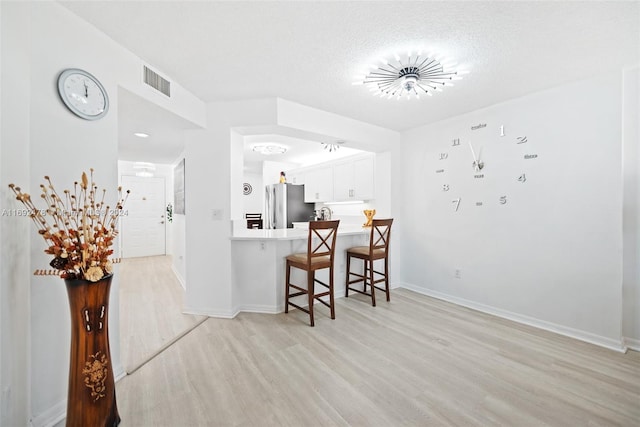 kitchen featuring white cabinets, a kitchen breakfast bar, light hardwood / wood-style floors, and stainless steel refrigerator