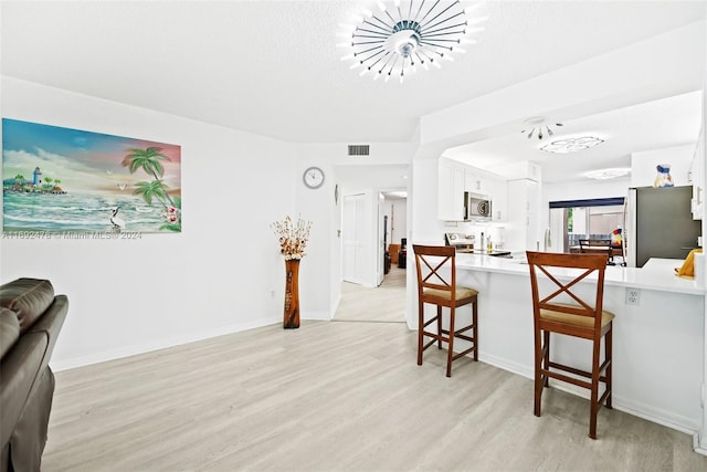 kitchen featuring appliances with stainless steel finishes, light hardwood / wood-style flooring, white cabinetry, and a kitchen breakfast bar