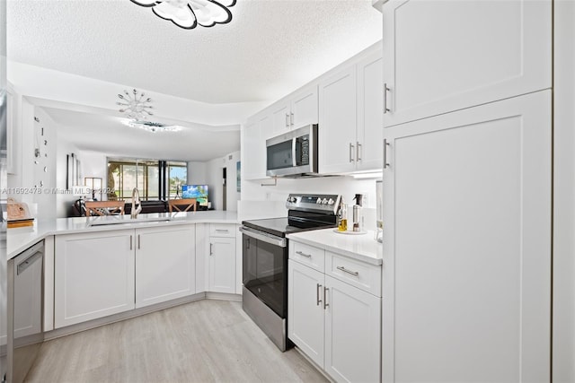 kitchen with sink, kitchen peninsula, a textured ceiling, white cabinetry, and stainless steel appliances