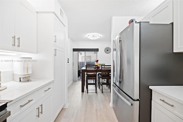 kitchen featuring light wood-type flooring, white cabinetry, a textured ceiling, and stainless steel refrigerator