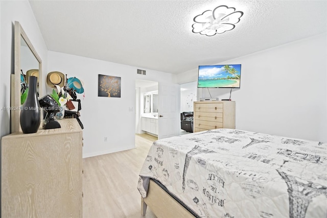 bedroom featuring a textured ceiling, connected bathroom, and light hardwood / wood-style flooring