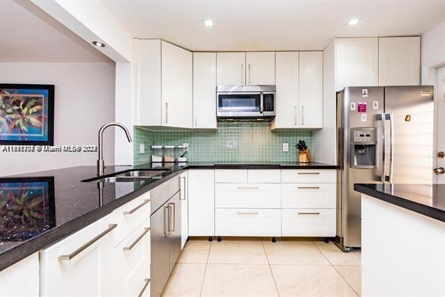 kitchen featuring sink, light tile patterned floors, white cabinetry, appliances with stainless steel finishes, and dark stone countertops