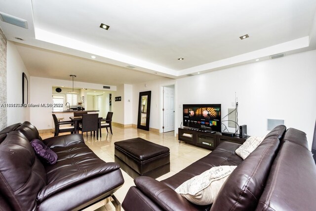 living room with sink, light tile patterned floors, and a raised ceiling