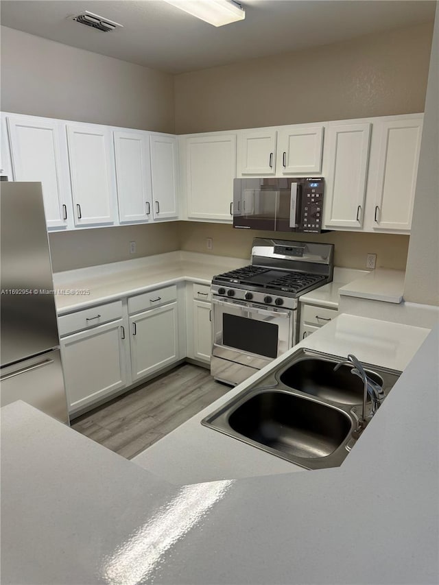 kitchen with white cabinets, appliances with stainless steel finishes, light hardwood / wood-style floors, and sink