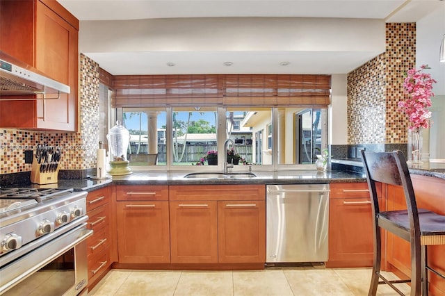 kitchen with appliances with stainless steel finishes, sink, range hood, dark stone counters, and tasteful backsplash