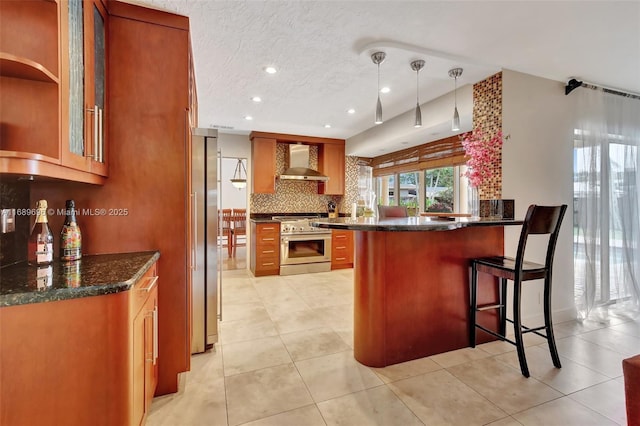 kitchen with a breakfast bar area, stainless steel appliances, wall chimney range hood, pendant lighting, and kitchen peninsula