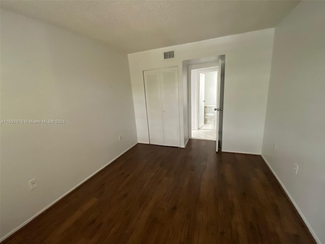 unfurnished bedroom with a closet, dark wood-type flooring, and a textured ceiling