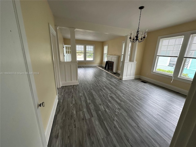 unfurnished living room with ornate columns, a chandelier, and dark hardwood / wood-style floors