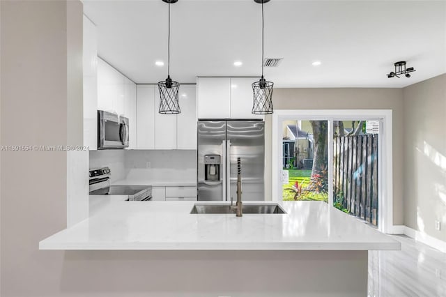 kitchen featuring stainless steel appliances, light stone counters, kitchen peninsula, white cabinetry, and decorative light fixtures