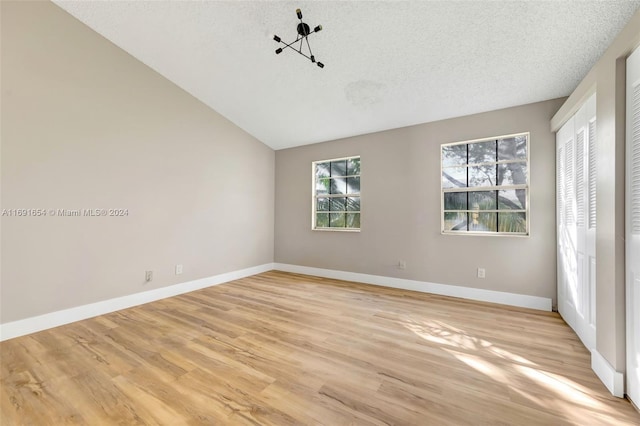 empty room featuring light wood-type flooring, a textured ceiling, and vaulted ceiling