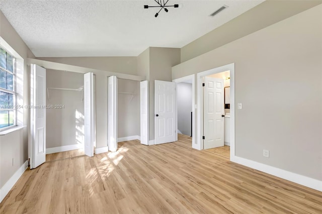 unfurnished bedroom with multiple closets, light hardwood / wood-style flooring, a textured ceiling, and vaulted ceiling