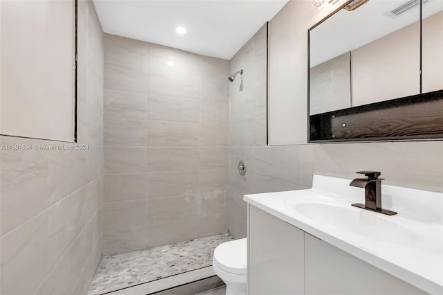 bathroom with tiled shower, tile walls, vanity, and toilet