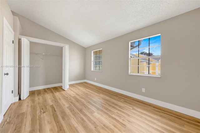 unfurnished bedroom featuring a textured ceiling, light hardwood / wood-style floors, multiple windows, and vaulted ceiling