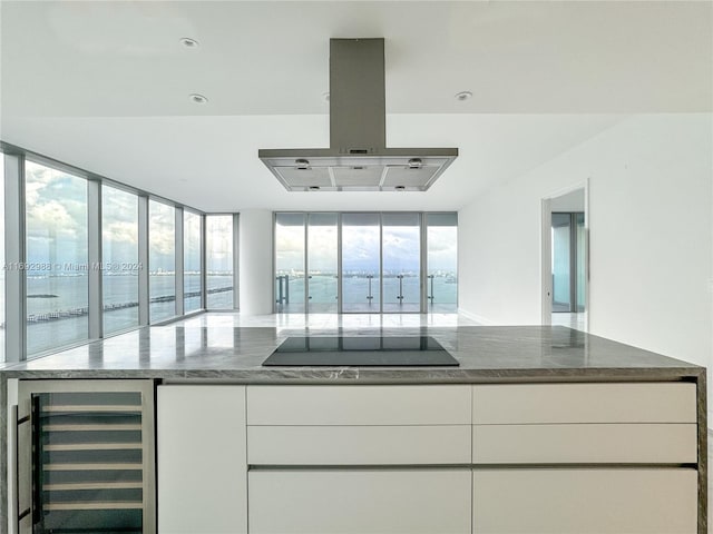 kitchen featuring floor to ceiling windows, beverage cooler, range hood, white cabinets, and black electric stovetop