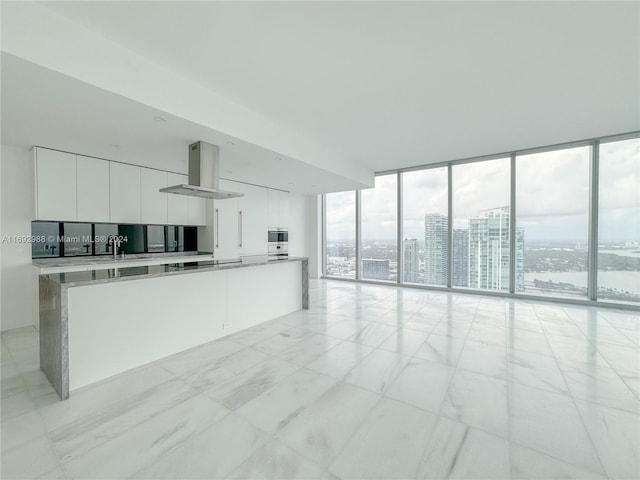 kitchen with white cabinets, wall chimney range hood, a kitchen island, backsplash, and a wall of windows