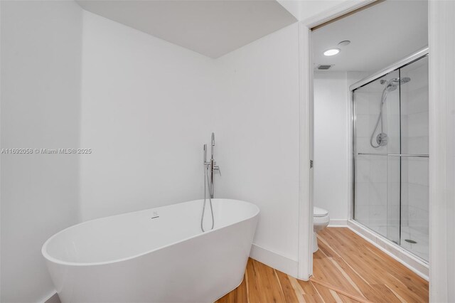 bathroom featuring toilet, wood-type flooring, and shower with separate bathtub