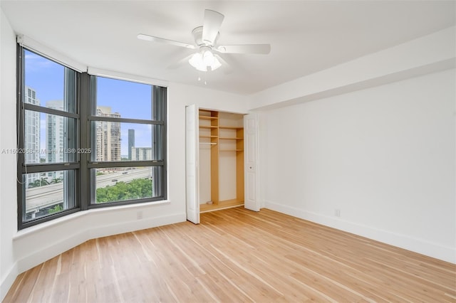 unfurnished bedroom with baseboards, a city view, ceiling fan, and light wood-style floors