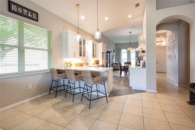 kitchen featuring decorative light fixtures, stainless steel refrigerator with ice dispenser, a breakfast bar, white cabinets, and kitchen peninsula