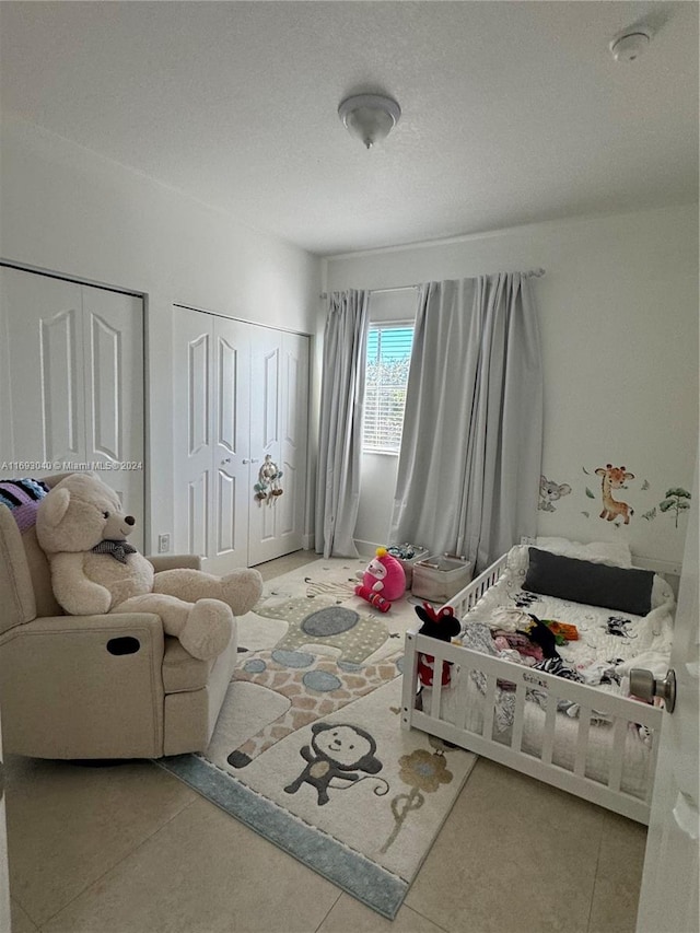 bedroom featuring tile patterned floors, multiple closets, and a textured ceiling