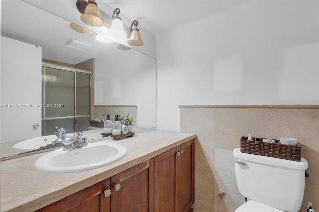 bathroom with a shower with shower door, vanity, toilet, and tile walls