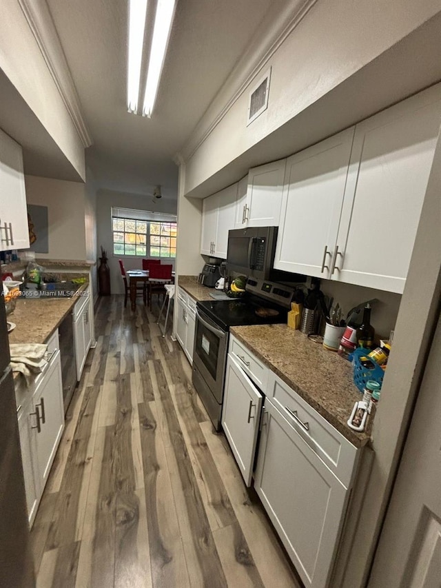 kitchen featuring hardwood / wood-style flooring, dark stone countertops, stainless steel range with electric cooktop, and white cabinets