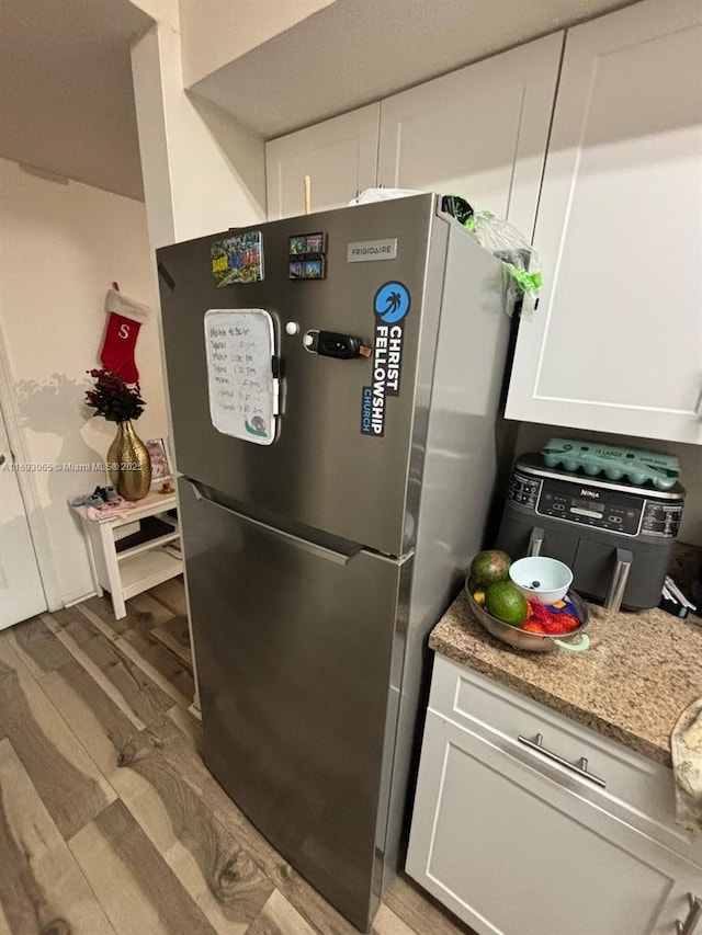 kitchen featuring hardwood / wood-style flooring, white cabinets, and stainless steel refrigerator