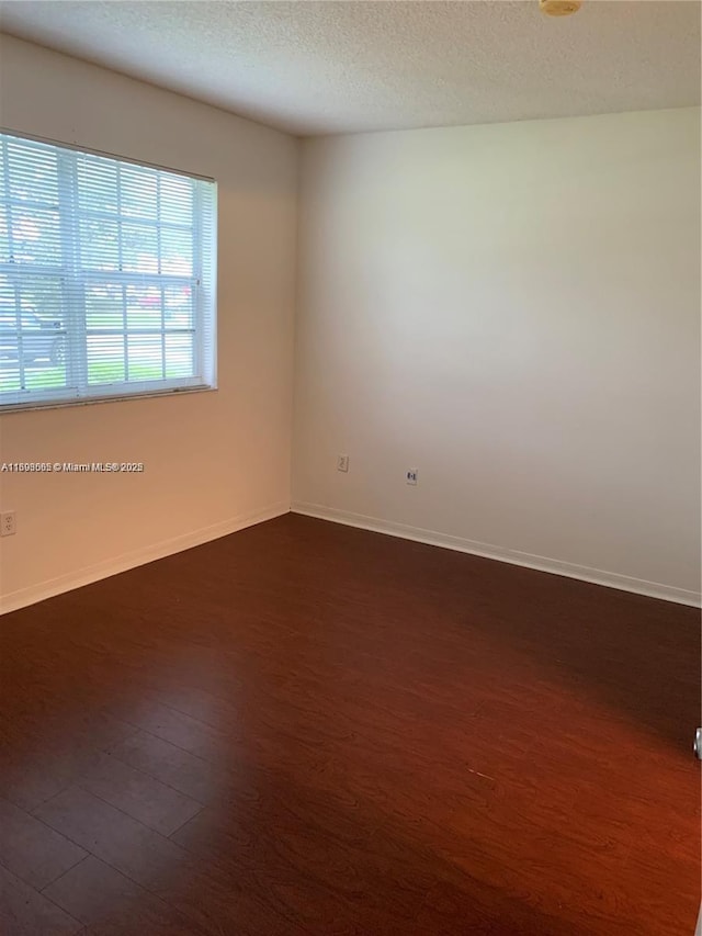 empty room with dark wood-type flooring and a textured ceiling