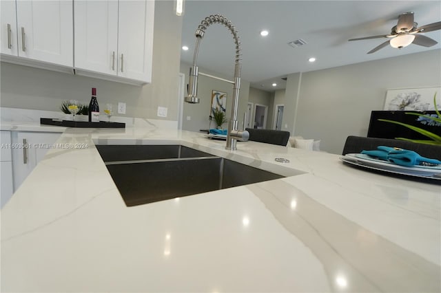 kitchen with light stone countertops, white cabinets, ceiling fan, and sink