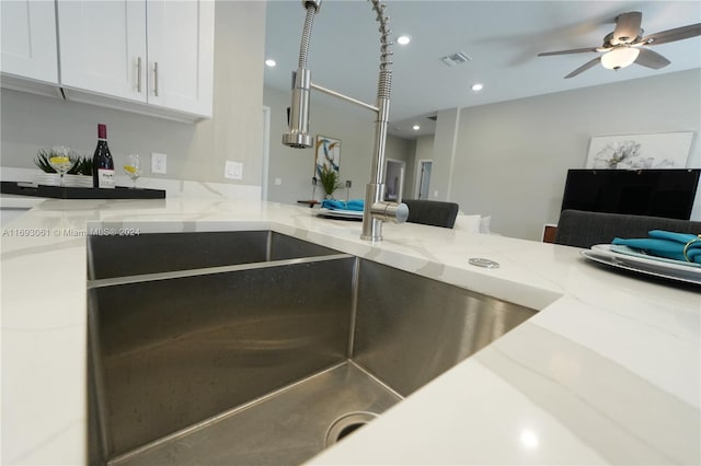 kitchen with white cabinetry, light stone counters, sink, and ceiling fan