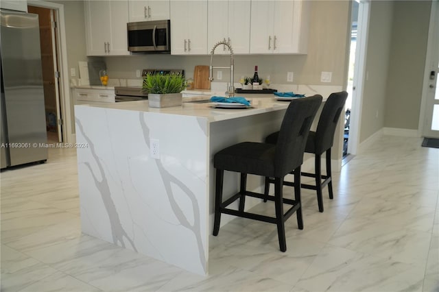 kitchen with white cabinets, appliances with stainless steel finishes, a kitchen breakfast bar, and sink