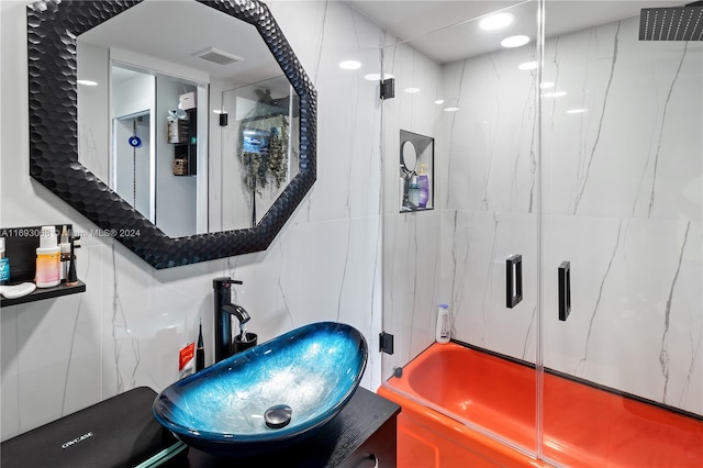 bathroom with tile walls, bath / shower combo with glass door, and sink