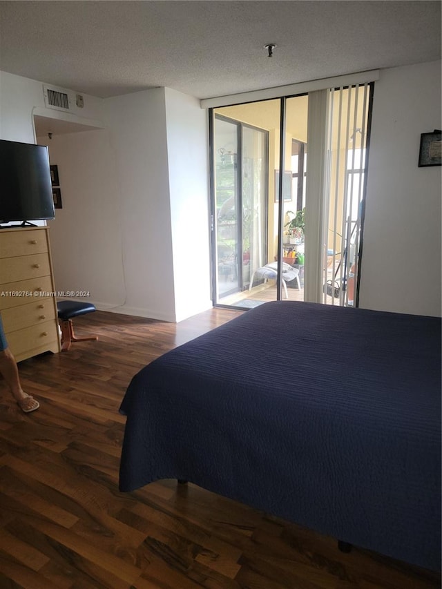 bedroom with expansive windows, dark hardwood / wood-style floors, a textured ceiling, and access to exterior