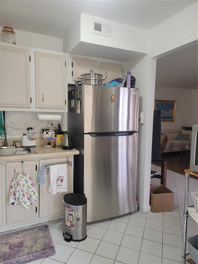 kitchen featuring sink, backsplash, stainless steel refrigerator, and light tile patterned floors