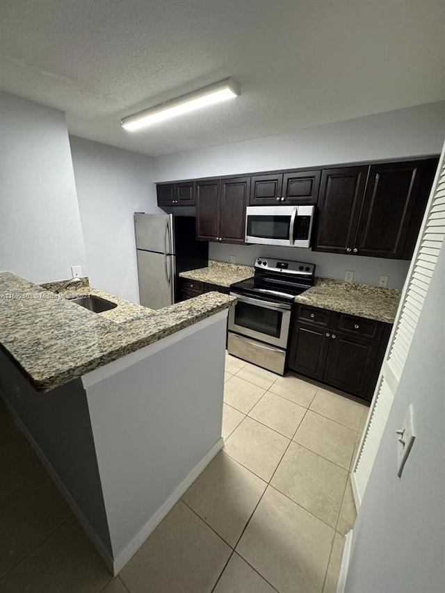 kitchen featuring sink, light tile patterned floors, dark brown cabinets, and appliances with stainless steel finishes