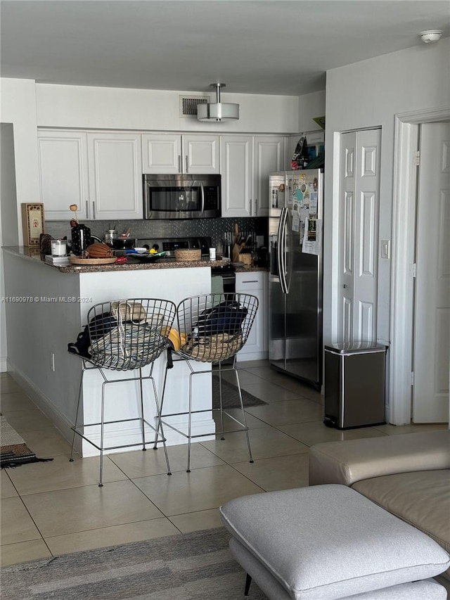 kitchen featuring stainless steel appliances, white cabinetry, backsplash, a kitchen breakfast bar, and kitchen peninsula