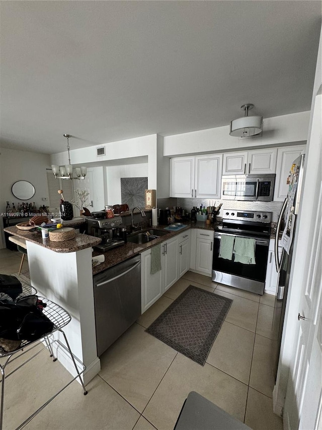 kitchen with white cabinetry, sink, kitchen peninsula, appliances with stainless steel finishes, and decorative light fixtures